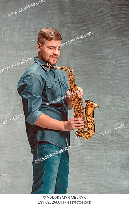Happy saxophonist with sax on gray studio background