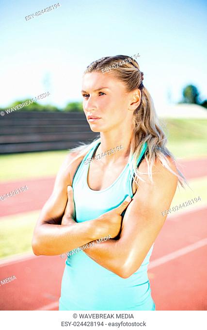 Female athlete standing with arms crossed on the running track