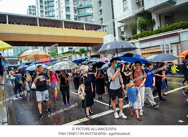 17 August 2019, China, Hongkong: Participants of a protest march run through the Hong Kong district of Kowloon and protect themselves with umbrellas from the...