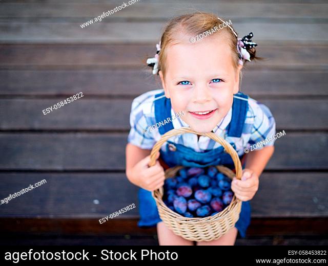 Little child girl gardener with basket full of plums