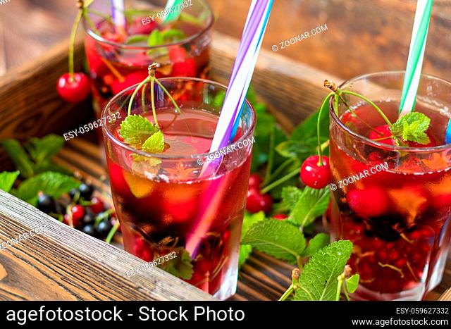 Glasses of refreshing drink flavored with fresh fruit and decorated with cherries covered with dew drops. Wooden background