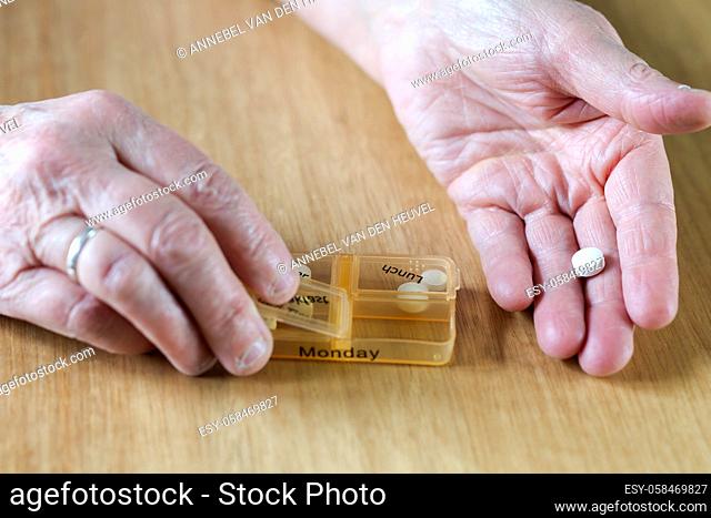 Closeup of an elderly senior woman's hands taking her medication for the week in a pill box on wooden table, business, health concept close up