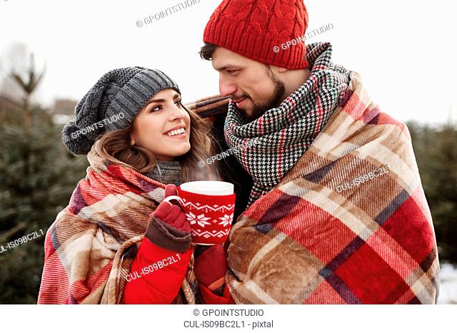 Romantic young couple wrapped in blanket while shopping for christmas tree from forest