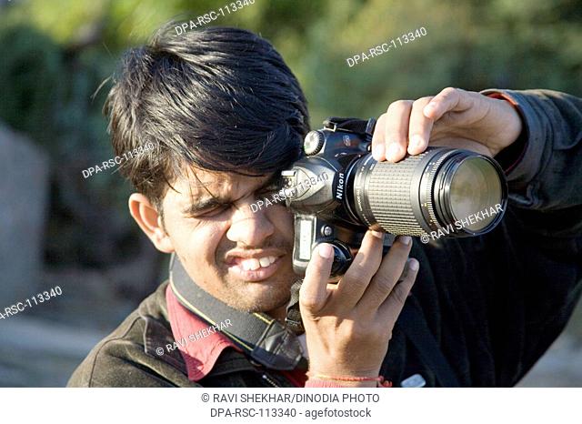 Photographer Pradeep shooting with digital camera zoom lens learning photography ; semi urban village Dilwara ; Udaipur ; Rajasthan ; India