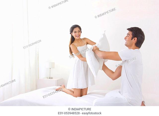 Excited young couple having pillow fight on bed