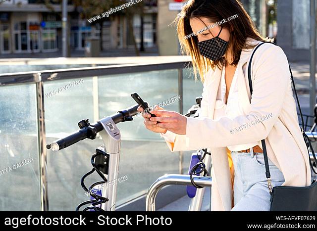 Young female entrepreneur doing contactless payment while standing at bicycle parking station