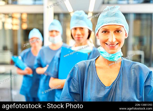 Lächelnde junge Chirurgin in blauer OP-Kleidung vor ihrem Chirurgie oder Notfall Team