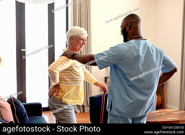 African american male health worker helping caucasian senior woman to walk using a walking stick