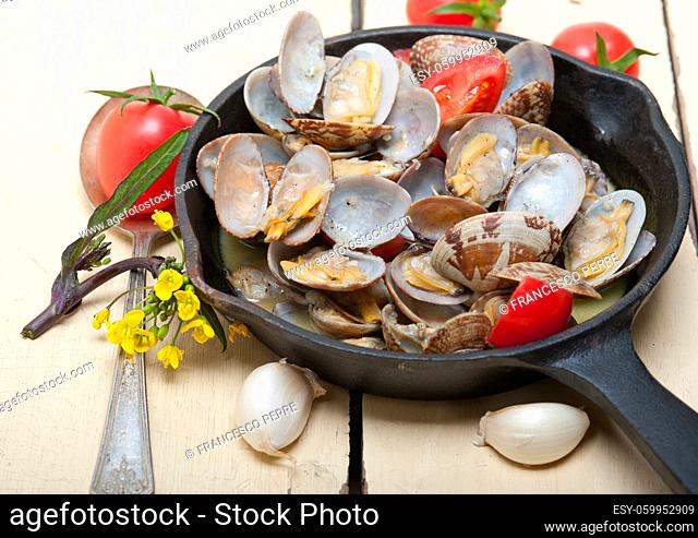 fresh clams stewed on an iron skillet over wite rustic wood table