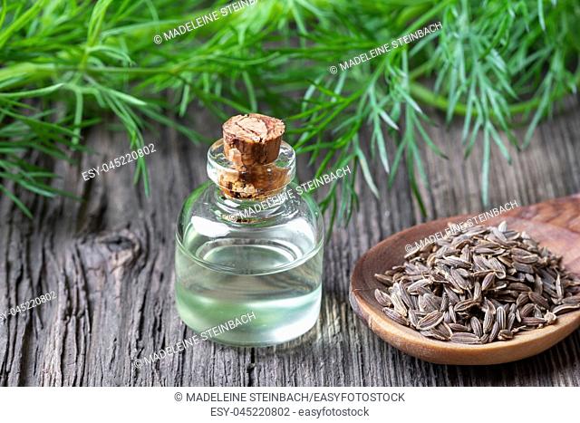 A bottle of essential oil with dill seeds and fresh leaves