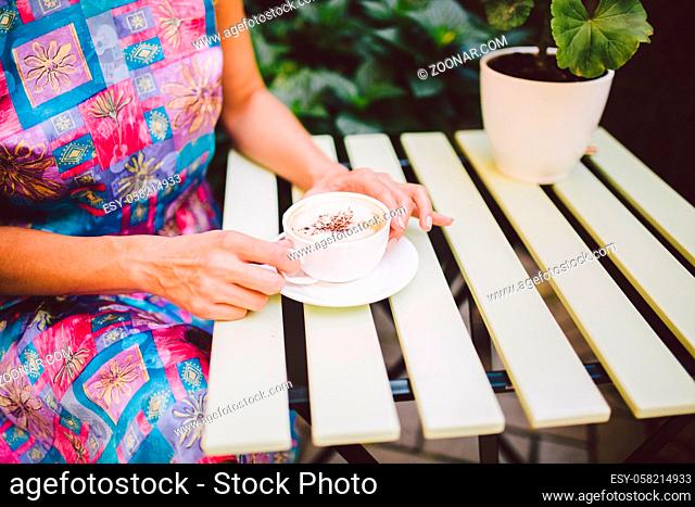 Close up image of woman shaking her favorite tasty chocolate cappuccino at cute cafeteria, wearing retro white skirt and accessorizes