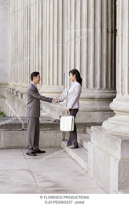 Two businesspeople outdoors on steps shaking hands