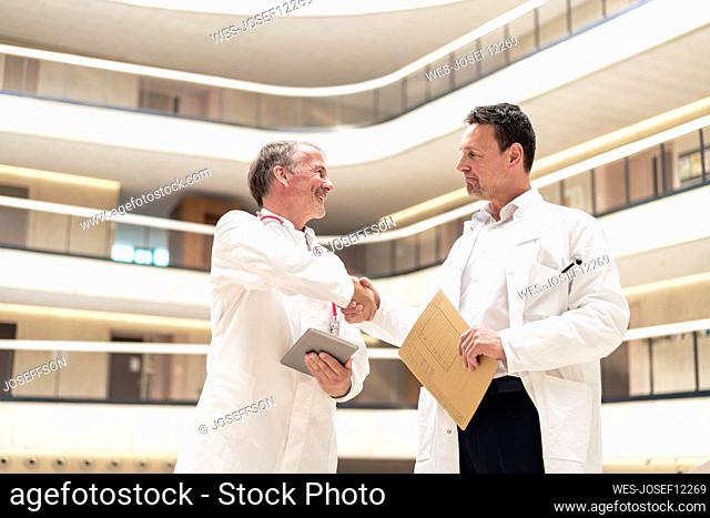 Doctor holding file shaking hand with colleague at hospital