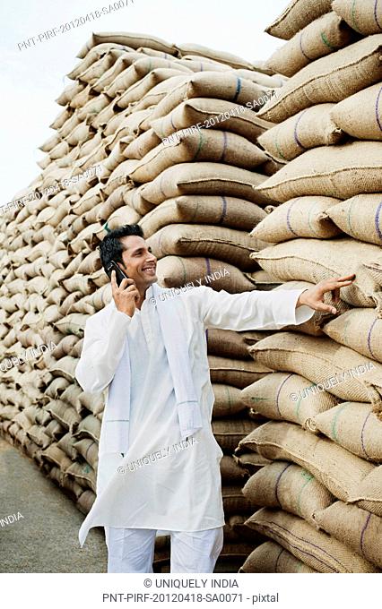 Man standing near sacks of wheat and talking on a mobile phone, Anaj Mandi, Sohna, Gurgaon, Haryana, India