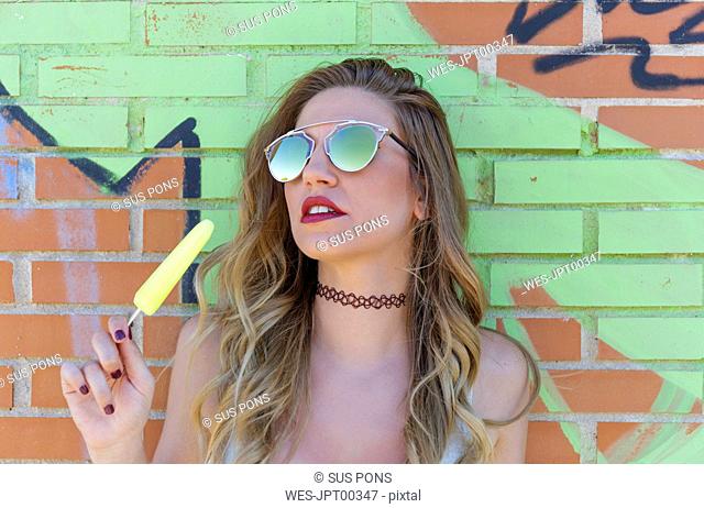 Portrait of young blond woman wearing sunglasses and holding a yellow popsicle