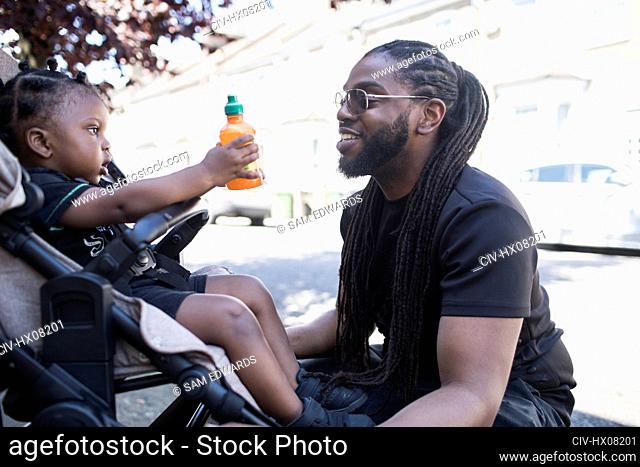 Father talking to toddler son in stroller on urban sidewalk