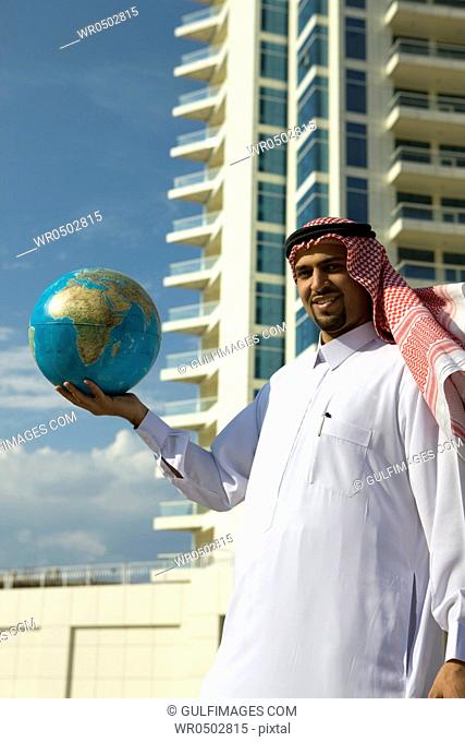 Arab man holding a globe, standing with background of building at Dubai Marina, UAE