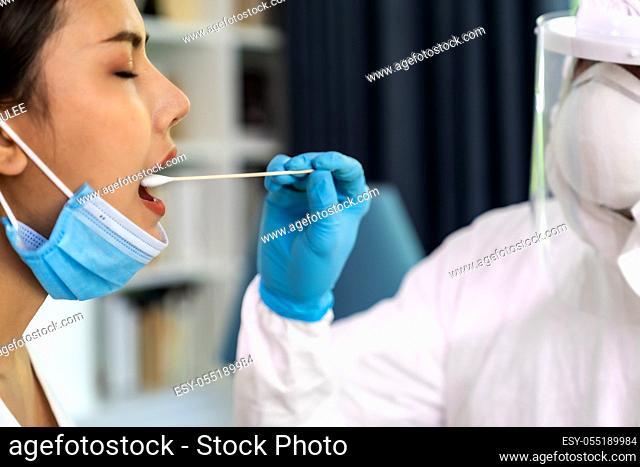 Medical staff with PPE suit test coronavirus covid-19 to asian woman by throat swab at home. New normal healthcare service at home and medical delivery concept