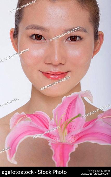 Portrait of young tranquil woman looking at camera with a large pink flower, studio shot