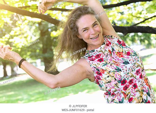 Portrait of happy mature woman wearing top with floral design dancing in a park