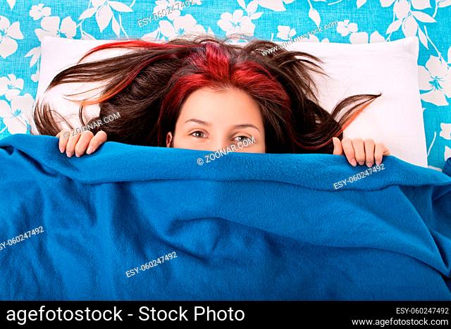 Good morning you... Beautiful young girl lying in bed, hiding her face behind a blanket