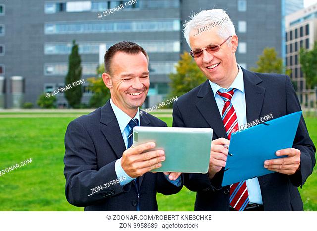 Zwei Geschäftsleute im Park schauen auf ein Tablet PC