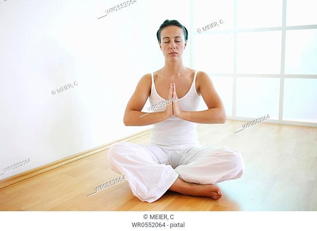 Young woman is sitting with crossed legs, folded hands and closed eyes on the floor