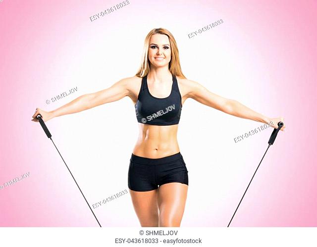 Fit, healthy and sporty woman in sportswear doing expander exercise pink background