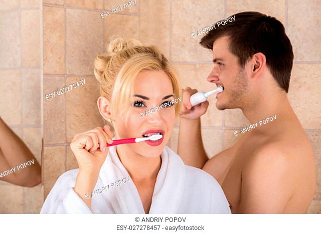 Portrait Of Man And Woman Brushing Teeth In Bathroom At Home