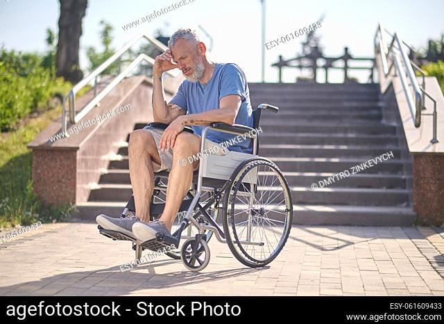 In thoughts. A disabled man in a wheel chair outdoors looking thoughtful