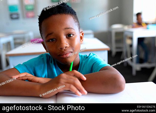 Portrait of african american elementary schoolboy sitting at desk in classroom