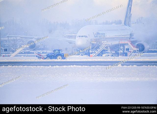 05 December 2023, Bavaria, Munich: A snow clearer drives in front of a plane in the snowstorm at the airport. After an interruption of several hours due to the...