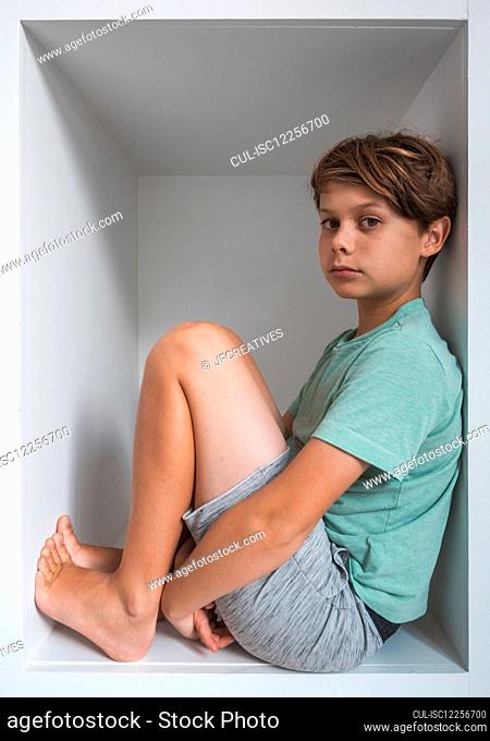 Portrait of brown haired boy sitting in closet, looking at camera