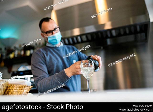 Waiter with face mask pouring wine in glass at counter