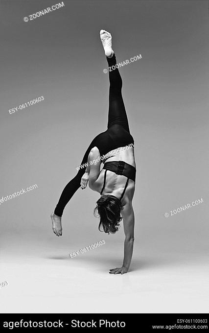 Beautiful young woman dancer making modern dancing elements. studio shot on grey background. copy space. monochrome