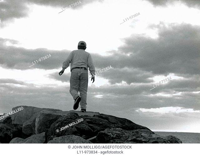 Boy on rocks, walking off towards clouds
