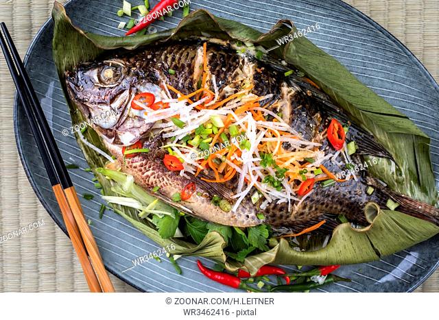 Traditional Thai barbecue tilapia fish with chili and vegetable as top view on a banana leaf