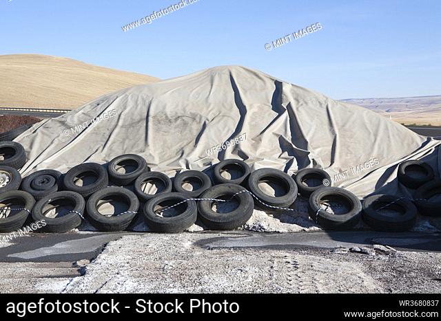 Heap of waste covered with tarpaulin, weighted down by rubber tires