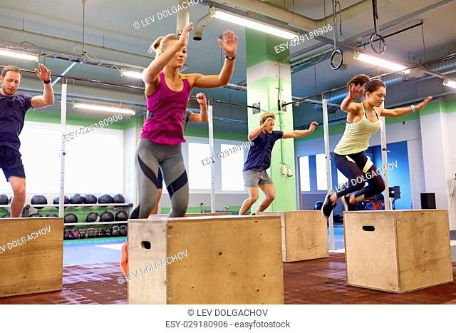 fitness, sport, training and exercising concept - group of people doing box jumps in gym (motion blurred image)