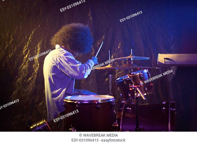 Male drummer with frizzy hair playing drum kit in nightclub