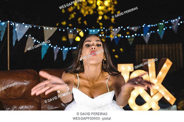 Portrait of happy bride blowing confetti on a night party outdoors