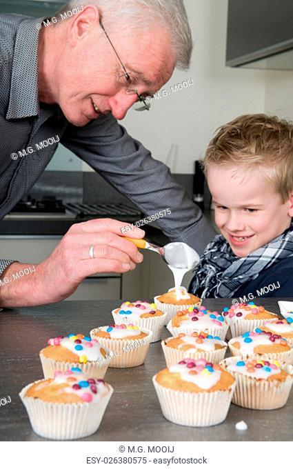 Grandpa and child are decorating the just baked cupcakes