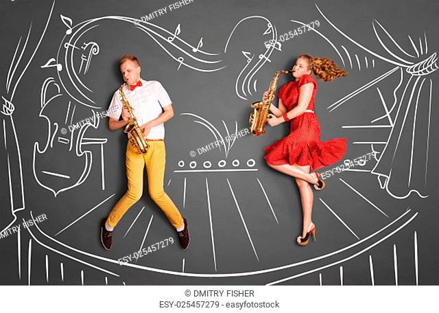 Love story concept of a romantic couple against chalk drawings background. Musician couple playing serenade on saxophone on stage