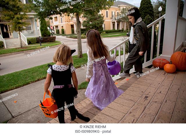 Boy and sisters trick or treating moving down porch stairway