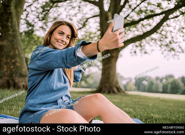 Smiling woman taking selfie through smart phone in park