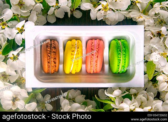 Spring branches of a blooming apple tree with white flowers and macaroons on a rustic wooden background, close-up