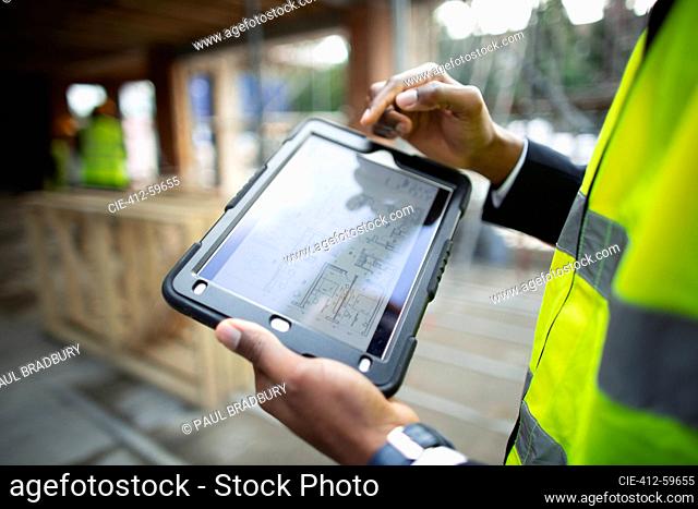 Male architect looking at blueprints on digital tablet