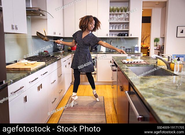 Ballet dancer standing on her toes and reaching for eggs while cooking in kitchen