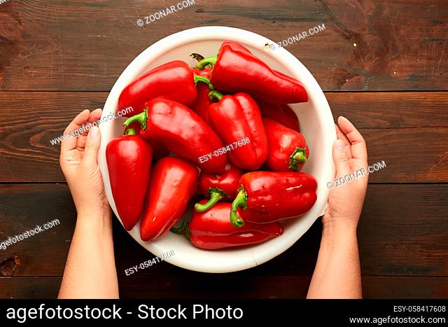 female hands holding a large white plastic bowl with red pepper, top view