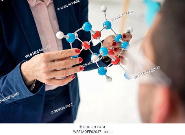 Businesswoman holding molecule model, teaching teenage boy